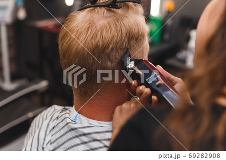 Female barber in mask cuts a man hairs with hair clipper. hairstyle during social distancing 69282908