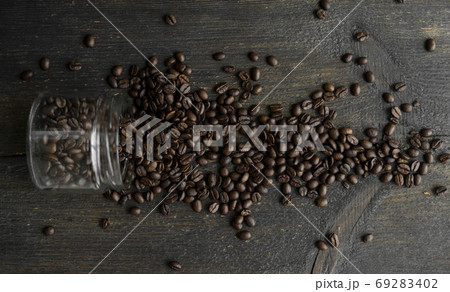Roasted fresh arabica coffee beans scattered on a table from a little jar on a wooden table. Fresh coffee beans. 69283402