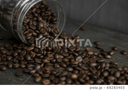 Roasted fresh arabica coffee beans scattered on a table from a little jar on a wooden table. Fresh coffee beans. 69283403