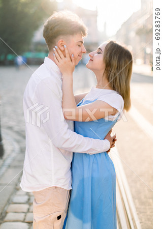 Lovely couple, boyfriendin white shirt and girlfriend in blue dress, looking at each other, smiling and hugging in old beautiful city in Europe. Couple, people, outdoor portrait concept 69283769