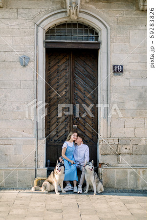 Happy couple with two husky dogs having fun outdoors in the city, sitting near ancient wooden door in front of old stone building. Full length photo Happy couple with two husky dogs having fun outdoors in the city, sitting near ancient wooden door in front of old stone building. Full length photo 69283826