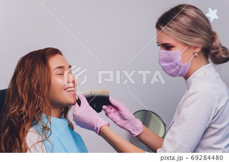 The dentist comparing patient's teeth shade with samples for bleaching treatment. 69284480