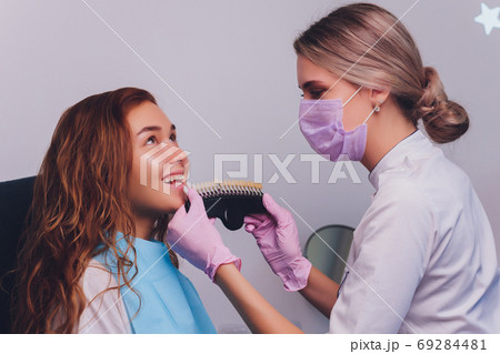 The dentist comparing patient's teeth shade with samples for bleaching treatment. 69284481