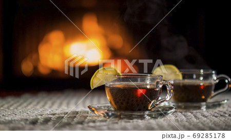 Two cups of tea with lemon on the background of the fireplace. Stand on a white knitted tablecloth Two cups of tea with lemon on the background of the fireplace. Stand on a white knitted tablecloth 69285178