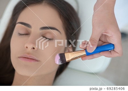 Cosmetologist applying facial mask on her customers face Cosmetologist applying facial mask on her customers face 69285406