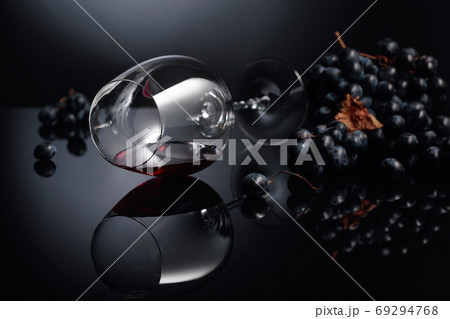 Blue grapes and wine glass with red wine on a black reflective b Blue grapes and wine glass with red wine on a black reflective b 69294768
