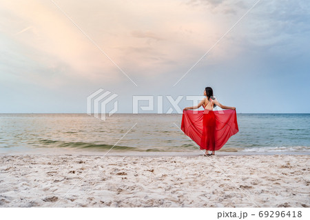 woman with arms spread in a red dress on the sea beach with wind 69296418
