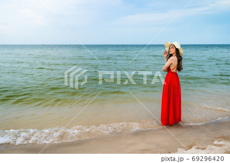 happy woman in red dress standing with arms crossed on sea beach 69296420