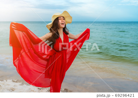 woman with arms spread in a red dress on the sea beach with wind 69296421
