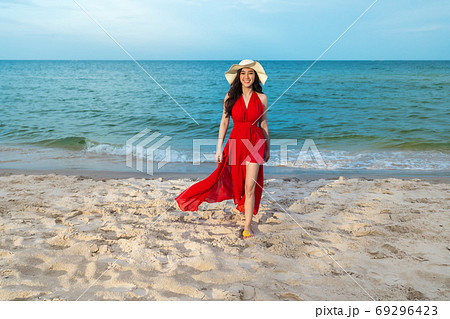 cheerful woman in red dress walking on sea beach 69296423