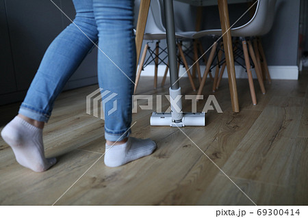 Woman holds white vacuum cleaner and drives it across floor 69300414
