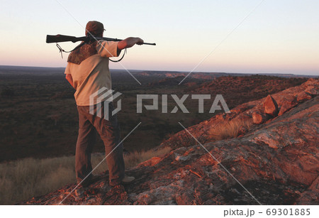 Hunter with  rifle on his shoulder looking down the mountain 69301885