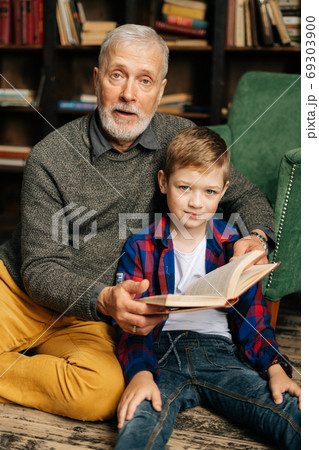 Portrait of happy child boy sitting with his grandfather and reading an interesting book Portrait of happy child boy sitting with his grandfather and reading an interesting book 69303900