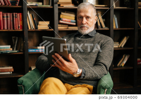 Portrait of confident bearded gray-haired mature adult male holding digital tablet in hand 69304000