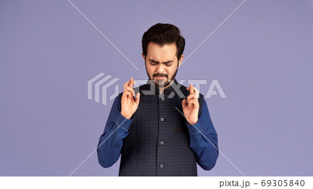 Making wish. Portrait of superstitious Indian guy keeping his fingers crossed on violet background Making wish. Portrait of superstitious Indian guy keeping his fingers crossed on violet background 69305840