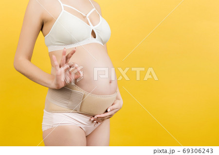 Close up of pregnant woman putting on a bandage at yellow backgr 69306243