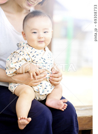 外でお母さんに抱っこされて恥ずかしそうに笑う赤ちゃんの写真素材