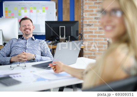 Man manager at work table sits smiling together with colleague Man manager at work table sits smiling together with colleague 69309351