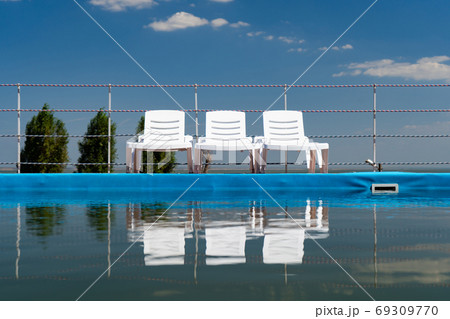 deckchairs on blue sky background stand near pool  69309770