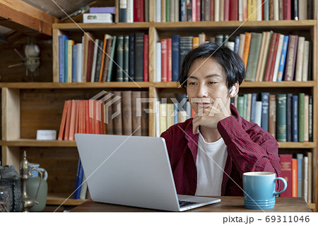 ワイヤレスヘッドホンをつけてパソコンで作業をする若い男性 ワイヤレスヘッドホンをつけてパソコンで作業をする若い男性 69311046