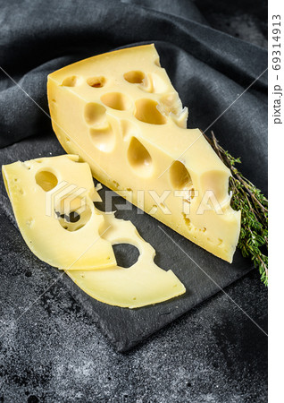 Piece of Maasdam cheese with large holes. Black background. Top view Piece of Maasdam cheese with large holes. Black background. Top view 69314913