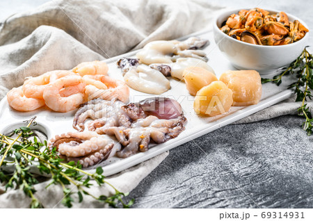 Raw seafood mix on a ceramic chopping Board. Gray background. Top view. Raw seafood mix on a ceramic chopping Board. Gray background. Top view. 69314931