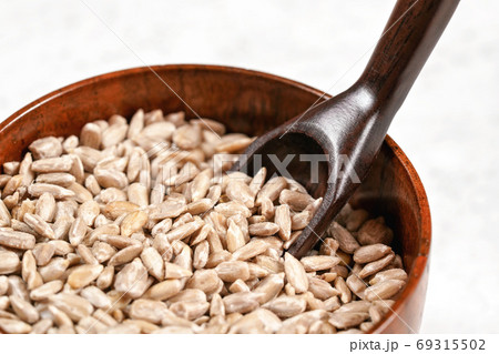 Peeled sunflower seeds in small wooden cup with little scoop, placed on white stone like board, closeup detail 69315502