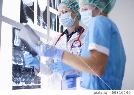 Doctors in medical office wearing protective medical masks and gloves and glasses are examining X-rays. 69316546