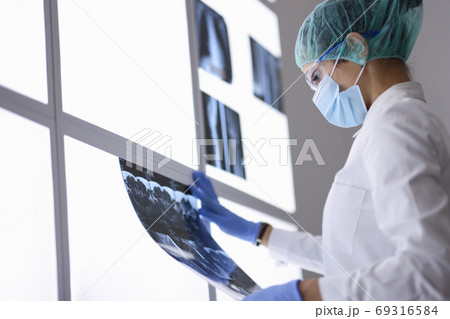 Doctor in protective medical mask and gloves examines an X-ray. Doctor in protective medical mask and gloves examines an X-ray. 69316584
