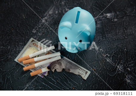 Blue piggy bank and cigarettes on dark table. Expensive habit 69318111