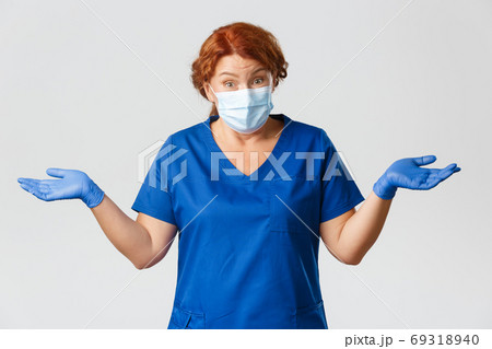 Medical workers, covid-19 pandemic, coronavirus concept. Confused and clueless redhead middle-aged female doctor, nurse being unaware, shrugging and spread hands sideways, wear face mask, gloves 69318940