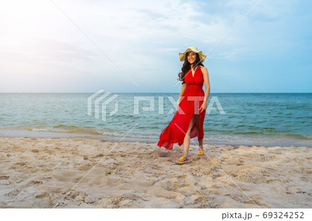 cheerful woman in red dress walking on sea beach 69324252