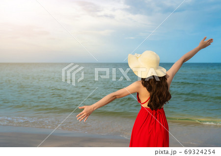 freedom woman in a red dress with arms raised on sea beach 69324254