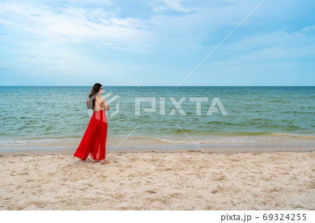 happy woman in red dress standing with arms crossed on sea beach 69324255