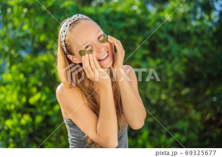 Smiling woman applying hydrogel eye care patches, moisturizing skin under eyes, enjoying skincare procedures 69325677