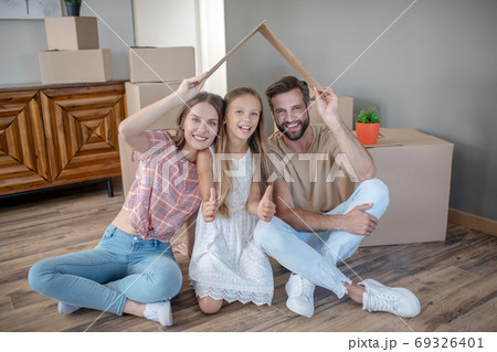 Family sitting under paper roof and smiling 69326401