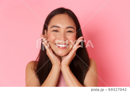 Beauty, fashion and lifestyle concept. Close-up of beautiful asian girl touching her face and smiling silly, blushing, feeling refreshed, apply skincare product or makeup, pink background Beauty, fashion and lifestyle concept. Close-up of beautiful asian girl touching her face and smiling silly, blushing, feeling refreshed, apply skincare product or makeup, pink background 69327042