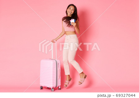 Travelling, holidays and vacation concept. Full-length of happy smiling asian girl, tourist with flight tickets and passport, jumping from excitement ready for summer paradise, pink background Travelling, holidays and vacation concept. Full-length of happy smiling asian girl, tourist with flight tickets and passport, jumping from excitement ready for summer paradise, pink background 69327044