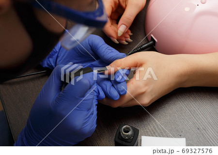 The master of nail service applies a transparent varnish to the clients nail. The master of nail service applies a transparent varnish to the clients nail. 69327576