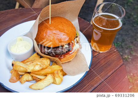 Delicious burger with french fries and a glass on beer on the wooden table Delicious burger with french fries and a glass on beer on the wooden table 69331206