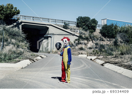 scary clown with a balloon and a knife outdoors 69334409