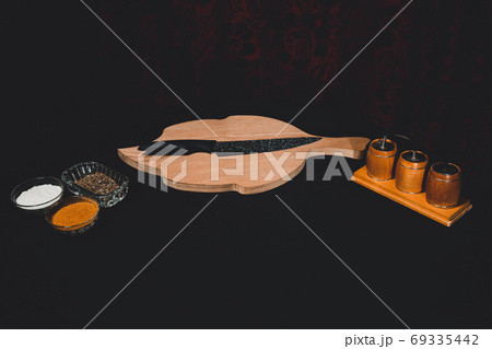 On a black background a wooden board with a black knife and a set of spices on kitchen utensils. On a black background a wooden board with a black knife and a set of spices on kitchen utensils. 69335442