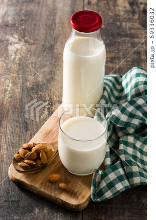 Organic almond milk in glass and bottle on wooden table.	 69336032