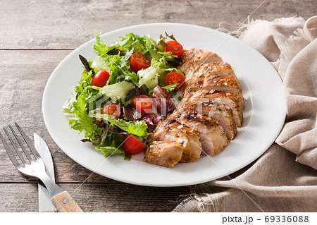 Grilled chicken breast with vegetables on a plate on wooden table. Grilled chicken breast with vegetables on a plate on wooden table. 69336088