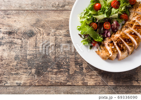 Grilled chicken breast with vegetables on a plate on wooden table. Grilled chicken breast with vegetables on a plate on wooden table. 69336090