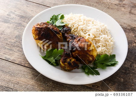 Roasted tandoori chicken with basmati rice in plate on wooden table.	 69336107