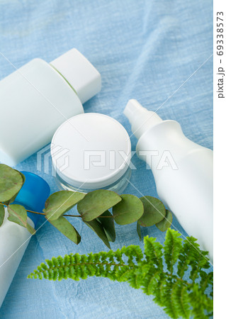 white cosmetic containers on a blue background decorated with green leaves. 69338573