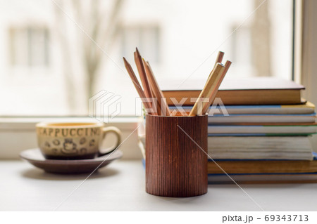 Cup of coffee, books, pencils in the pencil box on the windowsill in the morning 69343713