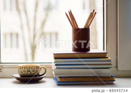 Cup of coffee, books, pencils in the pencil case on the window sill Cup of coffee, books, pencils in the pencil case on the window sill 69343714