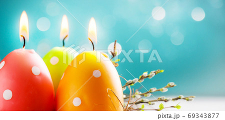 Easter colorful candle eggs with willow twigs on blurred blue background with bokeh lights. Copy space. Soft focus 69343877